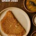 Golden brown instant wheat dosa served hot with coconut chutney, styled on a rustic brass plate.