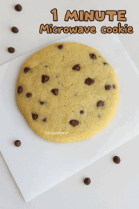 Top view of a single chocolate chip cookie made in a microwave, golden and crisp, placed on parchment paper with scattered chocolate chips.