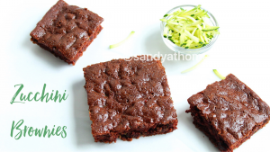 Eggless chocolate zucchini brownies styled with cocoa, grated zucchini, and a rustic linen background.