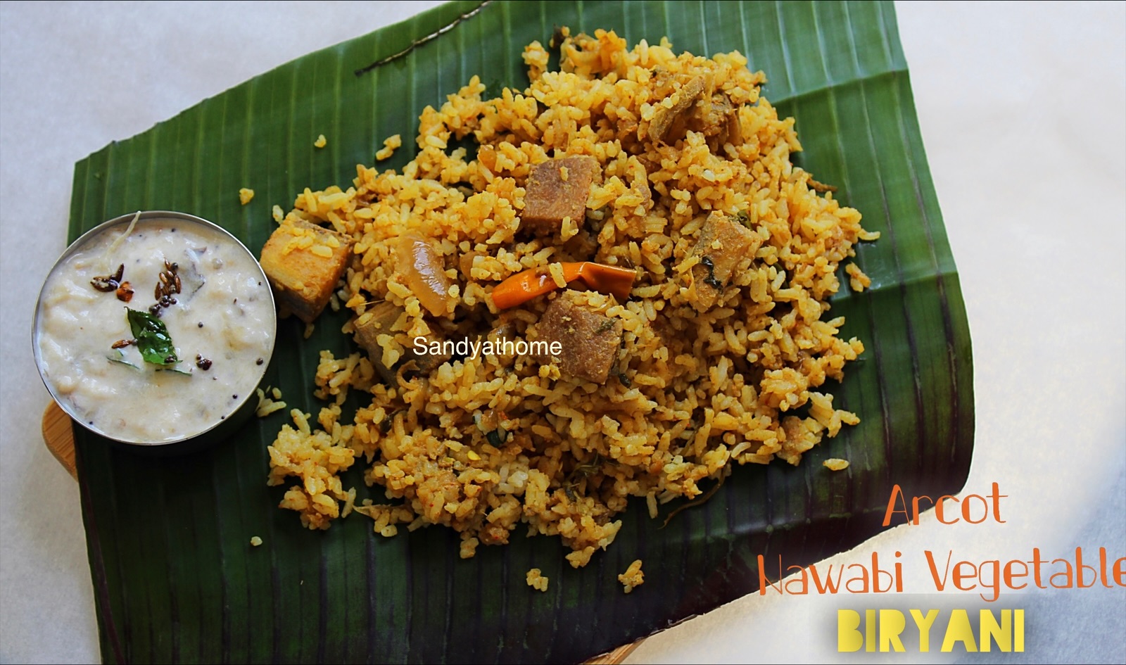 Rustic plated Arcot Nawabi Vegetable Biryani served on banana leaf, paired with authentic brinjal raita, representing Tamil-Mughal fusion cuisine.