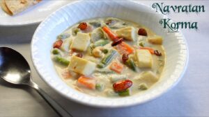 Close-up of restaurant-style Navratan Korma in white gravy with fried cashews, raisins, almonds, and paneer, styled for a festive Indian meal