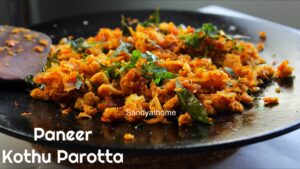 A close-up of South Indian paneer kothu parotta served on a brass plate, garnished with coriander and curry leaves