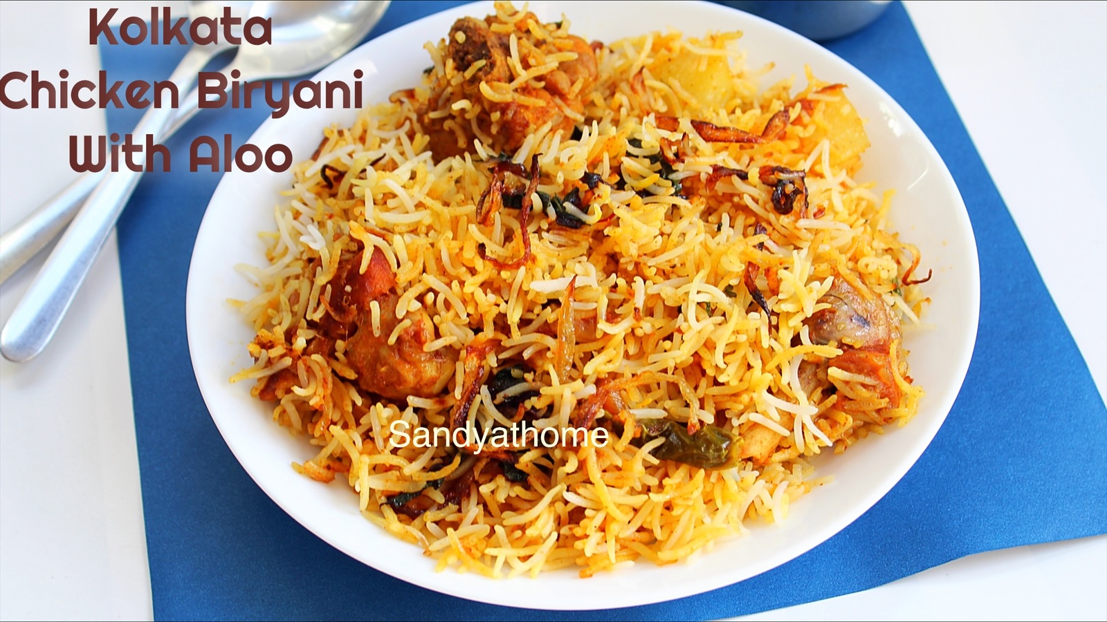 Chicken biryani with basmati rice, fried aloo, and chicken, neatly plated with raita and boiled egg on the side.
