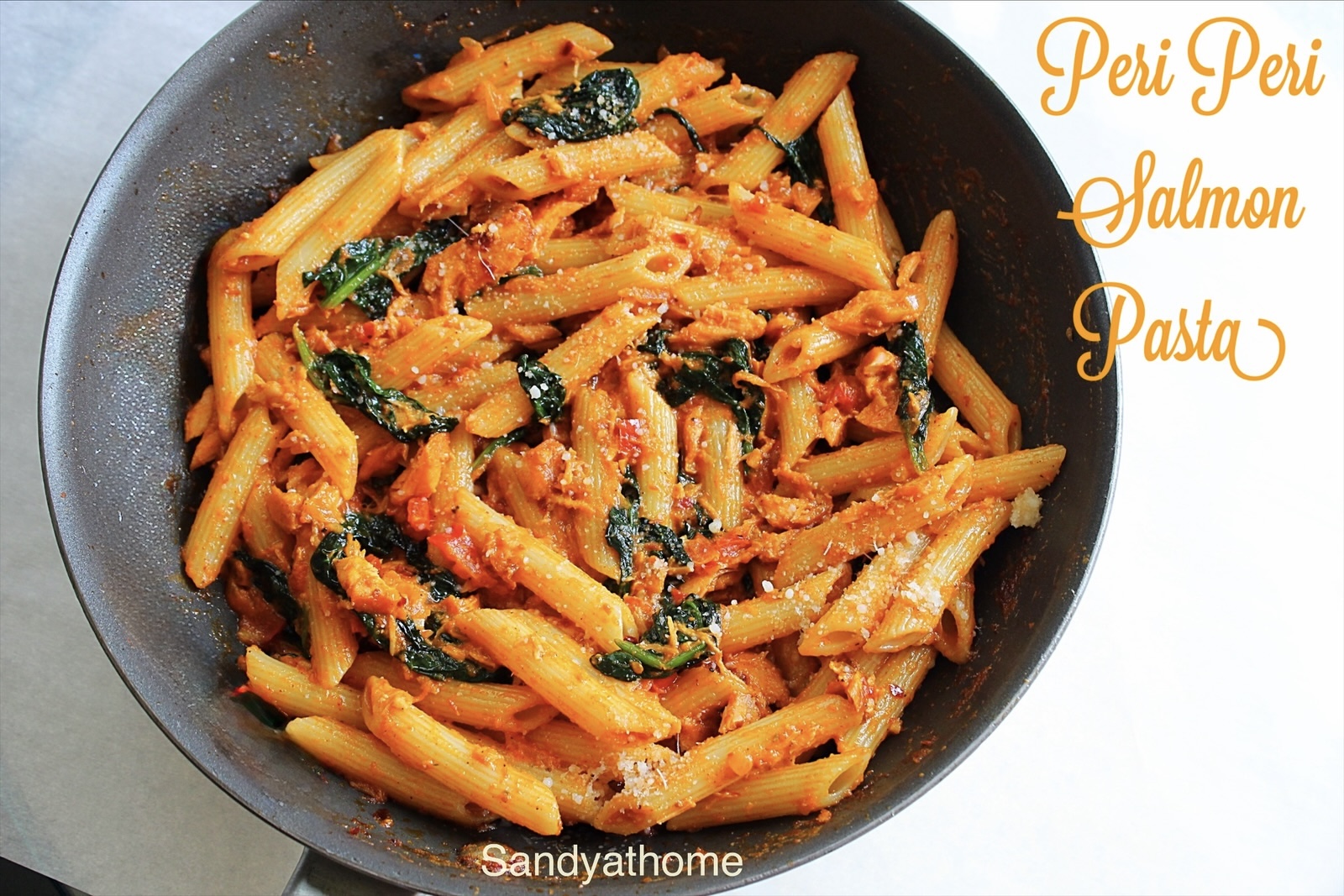 Creamy peri peri fish pasta served in a white bowl with seared salmon, spinach, and rich tomato cream sauce.
