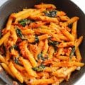 Bowl of peri peri salmon pasta with wilted spinach and chili flakes, ready for serving.