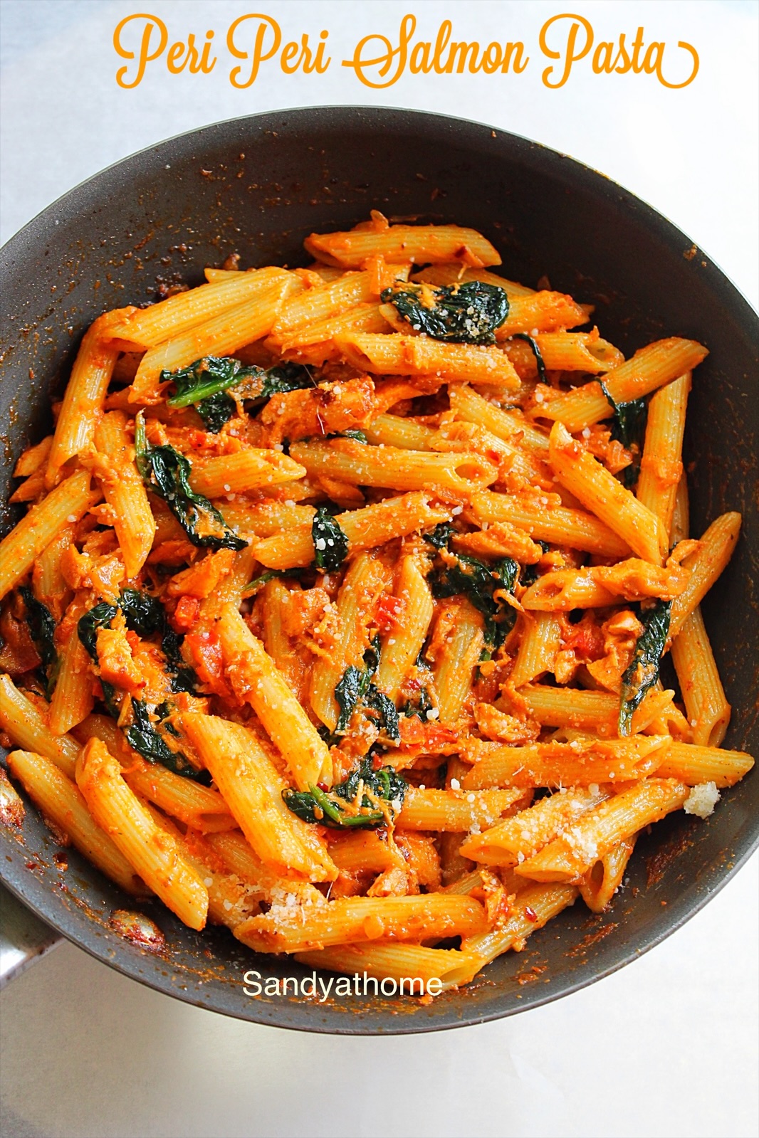 Bowl of peri peri salmon pasta with wilted spinach and chili flakes, ready for serving.