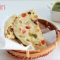 Homemade Kashmiri naan topped with tutti frutti, almonds, and cashews served warm on a plate.