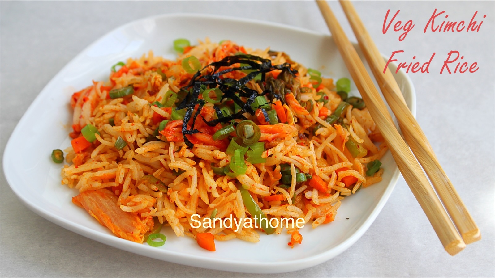 Close-up of veg kimchi fried rice garnished with roasted seaweed strips, spring onions, and sesame oil drizzle.