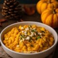 Overhead view of a rustic bowl filled with butternut squash pasta, garnished with feta and herbs, placed on a wooden surface with linen and cutlery — warm autumn comfort food.