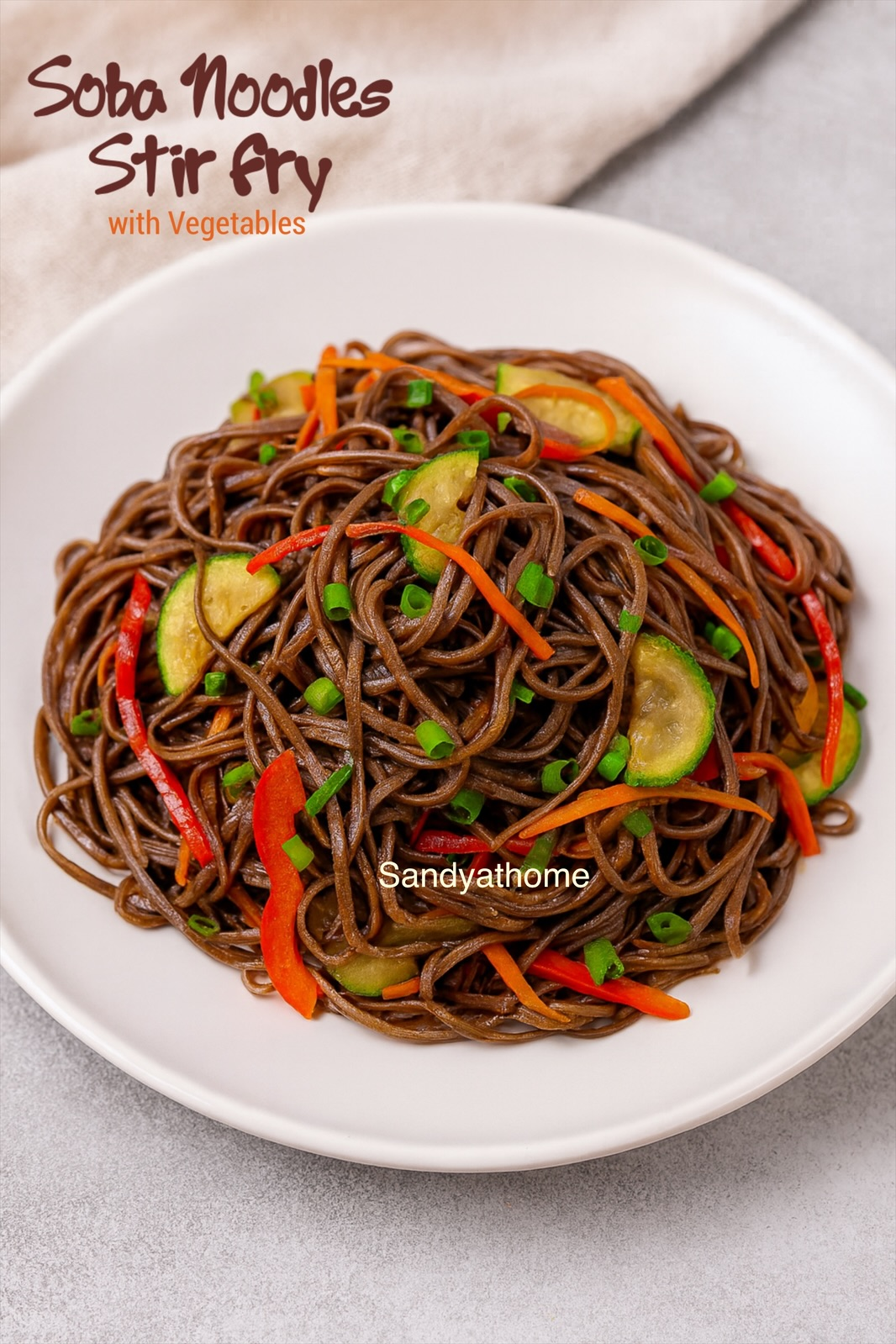 A bowl of colorful vegetable soba noodles tossed in soy-sesame sauce with bell peppers, carrots, and zucchini served on a rustic wooden background.